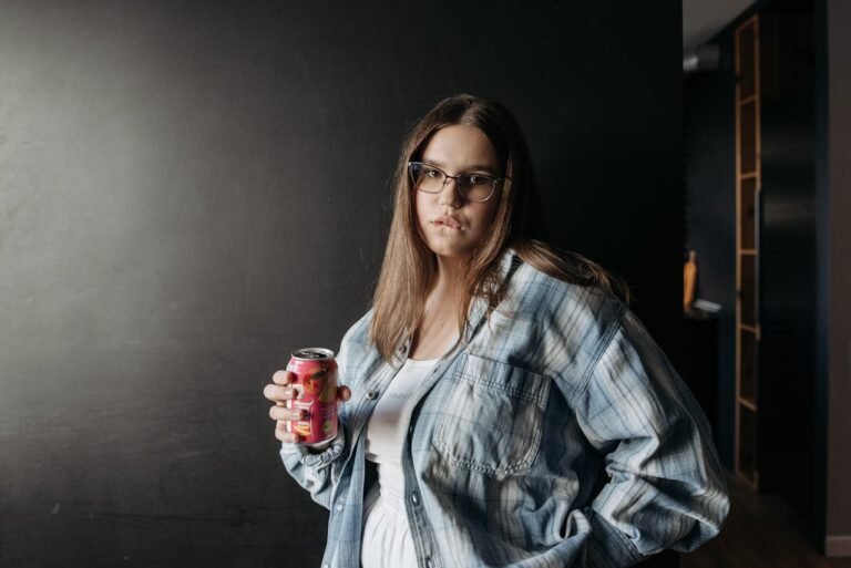 Une femme en manches longues à carreaux tenant une canette de soda tout en regardant la caméra