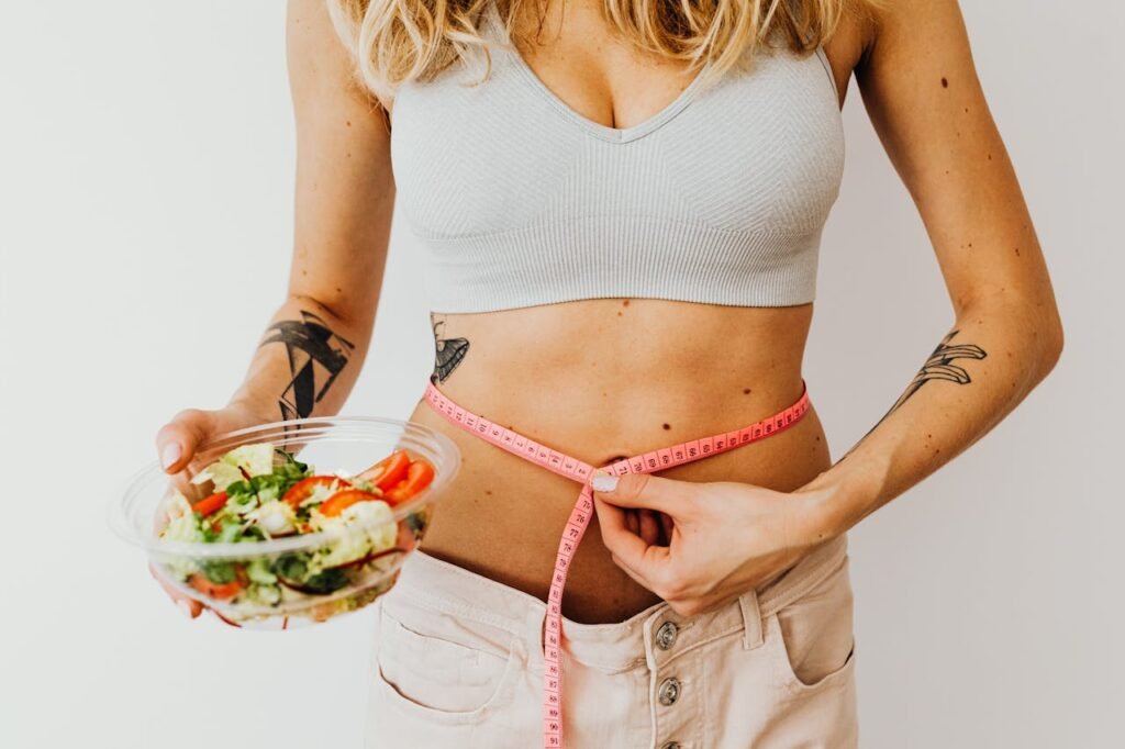 Femme en soutien-gorge de sport tenant un ruban à mesurer et un bol de salade