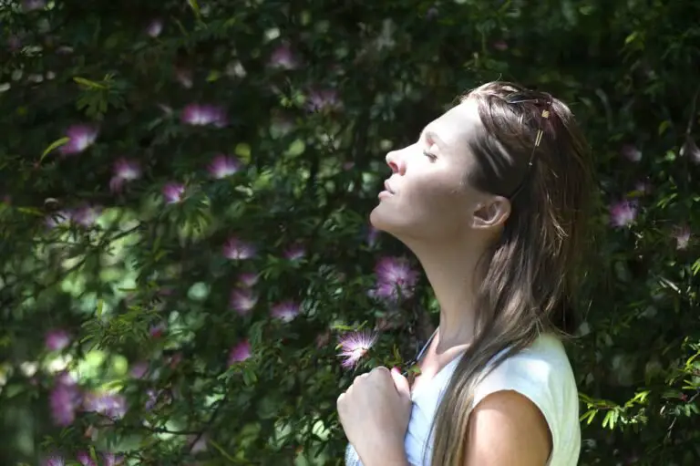 Femme fermant les yeux contre la lumière du soleil debout près d'une plante à fleurs aux pétales violets