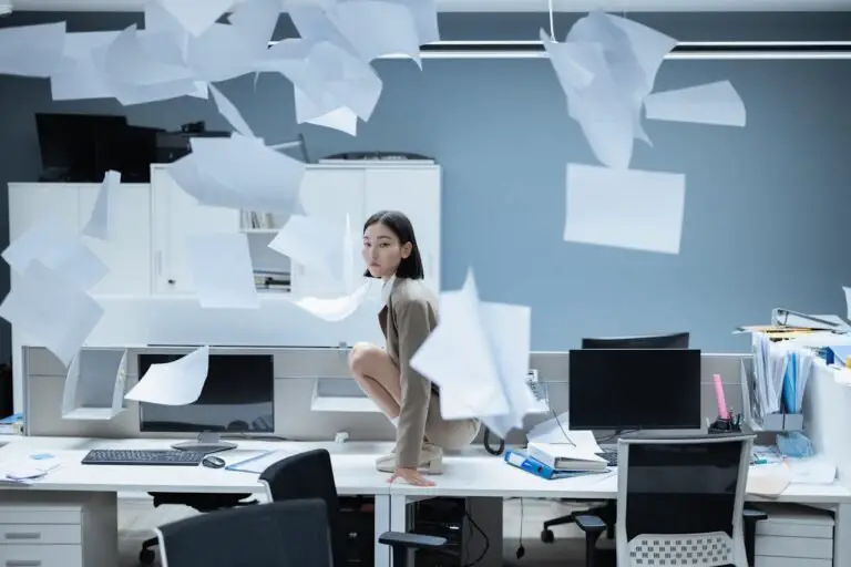 Stress au bureau - Femme accroupie sur un bureau parmi des papiers volants